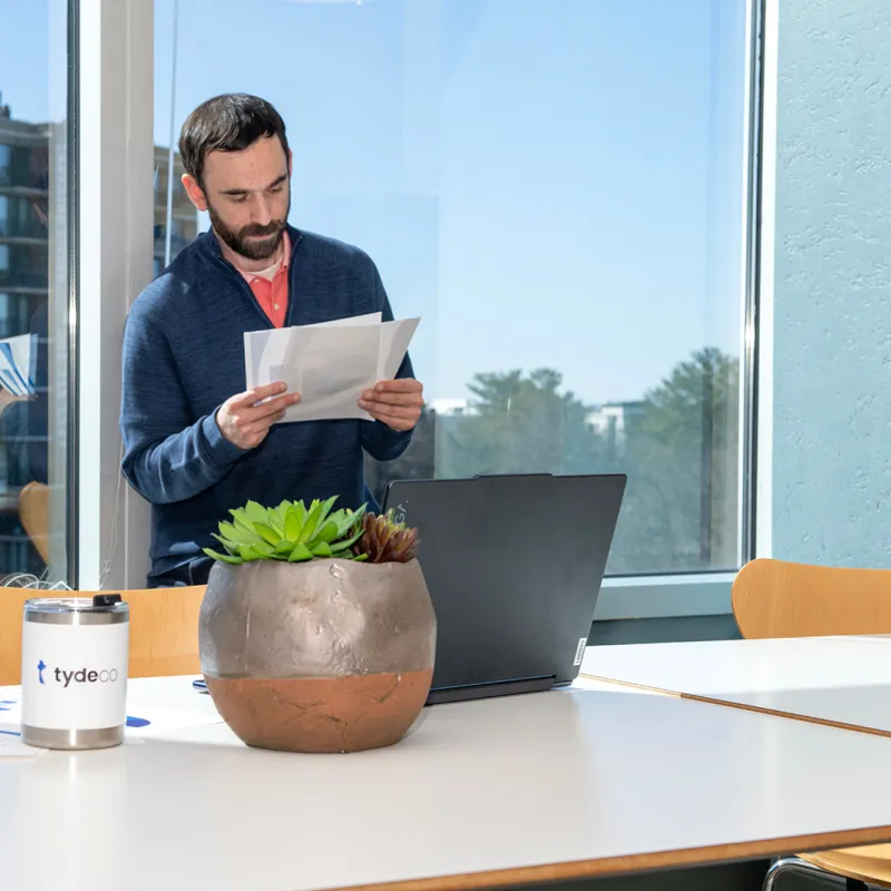 man looking at documents standing in an office in front of a laptop