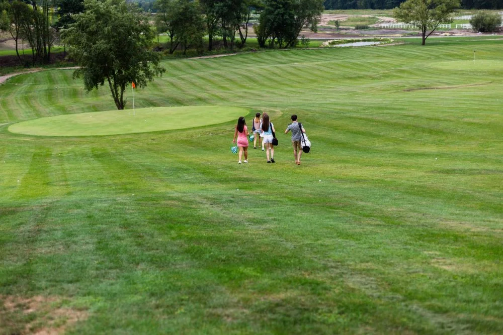 Group of people walking across a green golf course toward a flag on a sunny day.