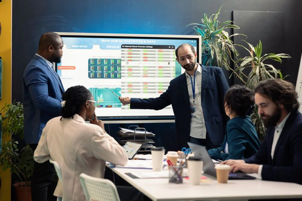 Business team in a meeting reviewing data and charts on a large digital screen in a modern office.