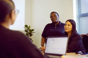 Colleagues listening during a meeting with a laptop open on the table in a bright office.