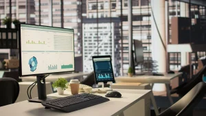 Office desk with monitor showing financial dashboards, representing Artisan Talent’s improved visibility & control after partnering with TydeCo™