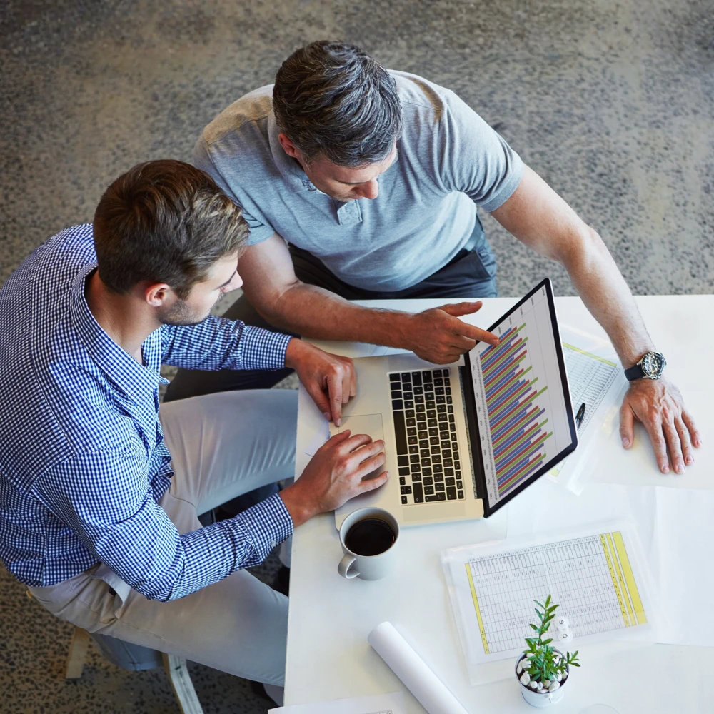 Two accounting professionals reviewing financial data and colourful charts on a laptop.