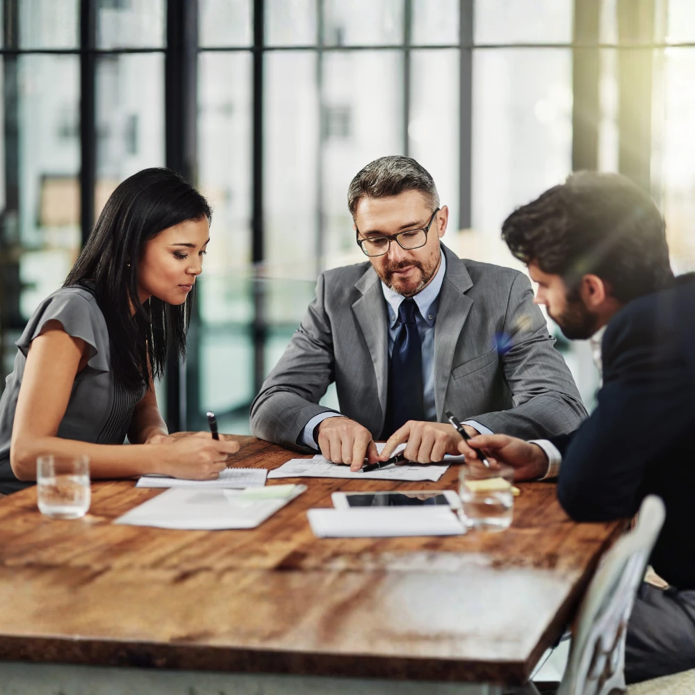 Three lawyers seated at a conference table reviewing financial reports and discussing law firm partnership planning.